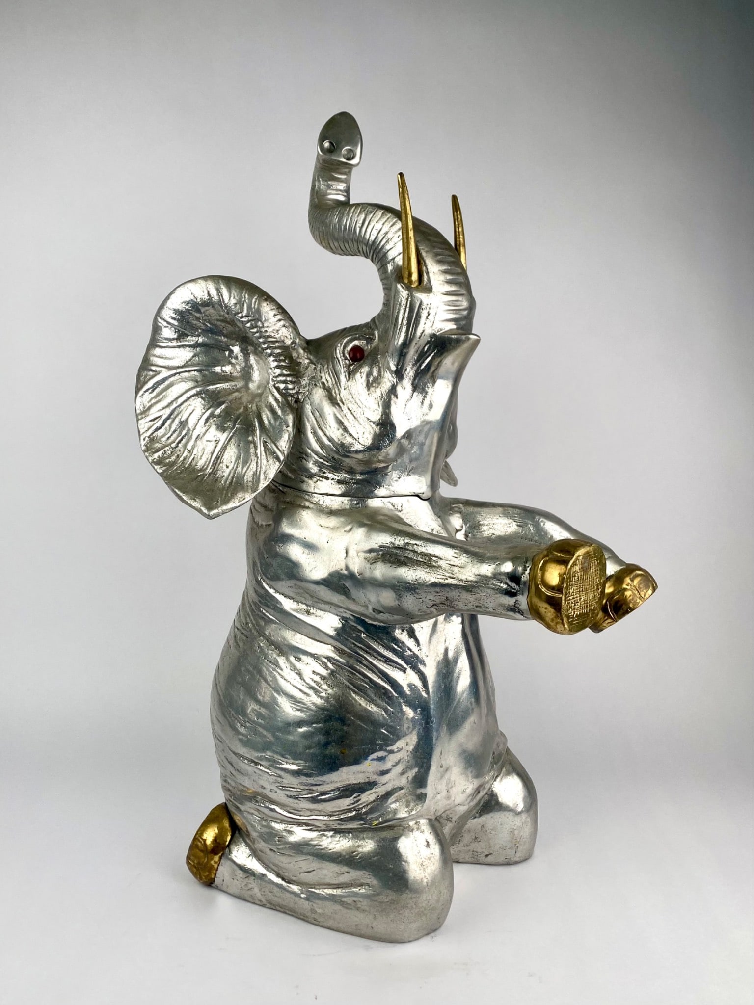 Figural elephant form barware vessel designed as an ice or wine bucket by Arthur Court. The piece: Figural elephant form barware vessel designed as an ice or wine bucket by Arthur Court. The piece depicts a seated elephant with raised trunk, red glass eyes, and gilt-tone tusks and feet, finished in