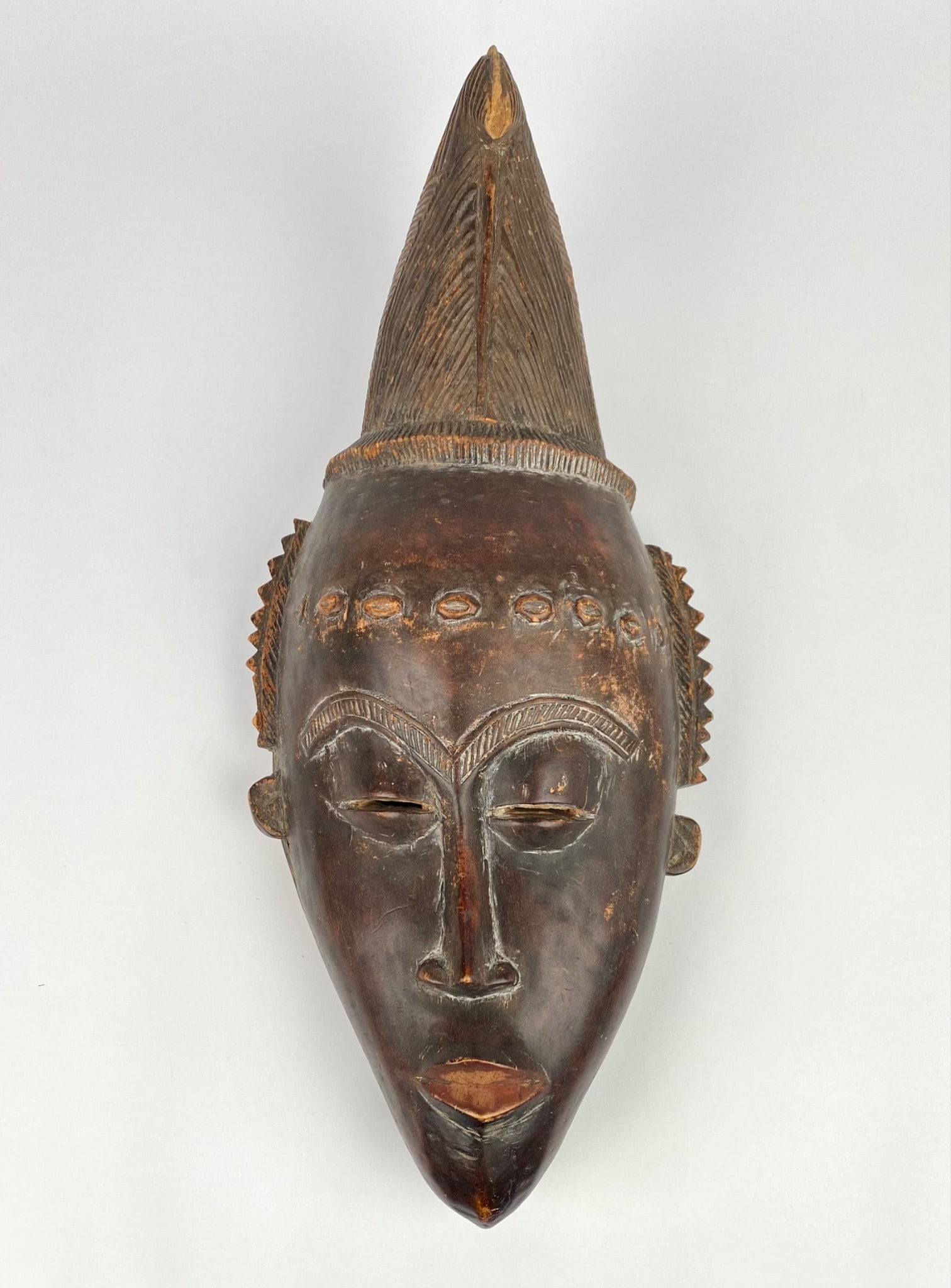 Carved Baule-style wooden mask featuring an abstract facial design with emphasized brows and mouth, (1 of 6)