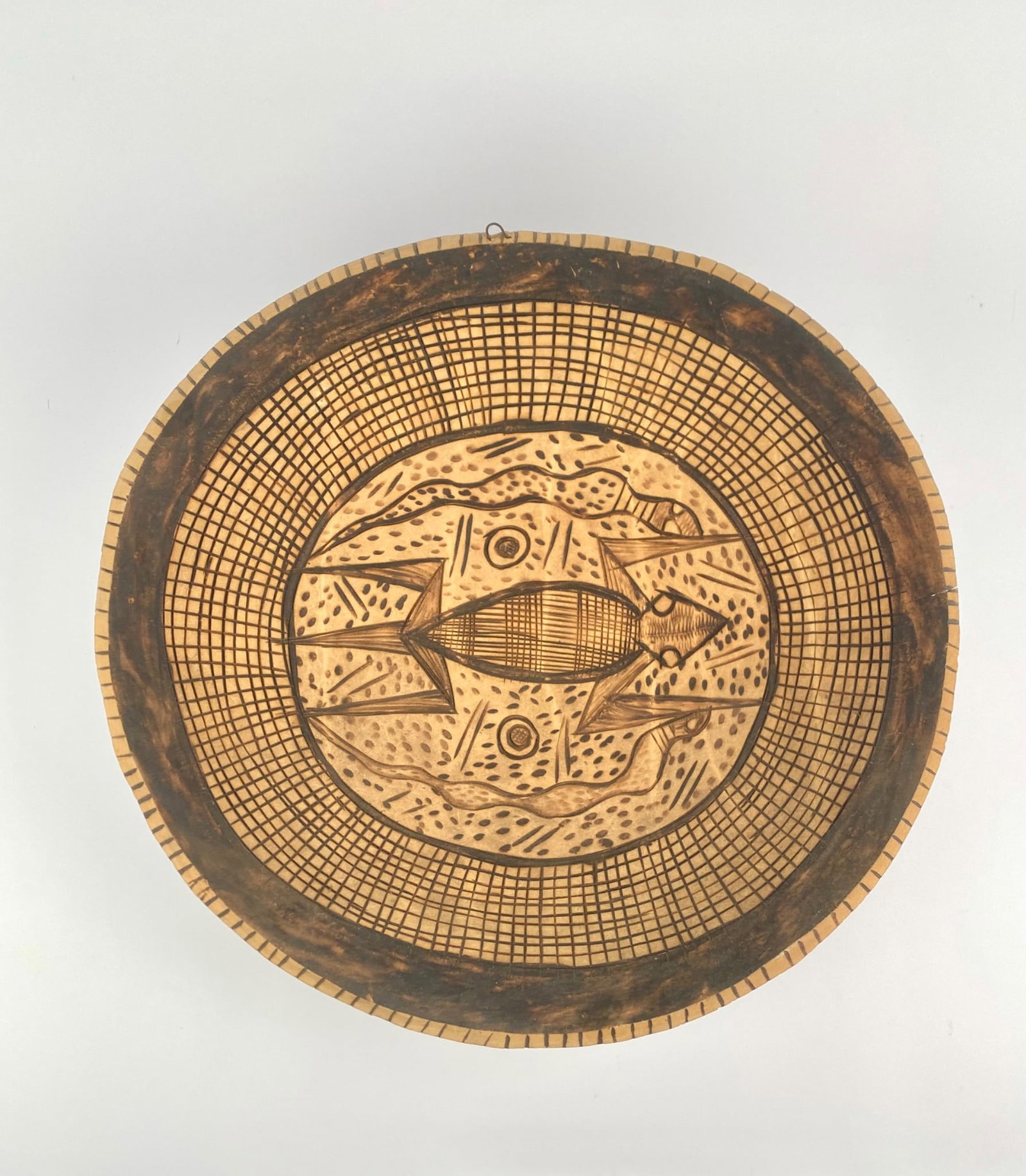 African Hand-Carved Wooden Wall Platter with Figural Motifs: Hand-carved African wooden wall platter featuring a bold figural composition surrounded by geometric decoration. The central field depicts a stylized anthropomorphic form. The carving exhibits varied