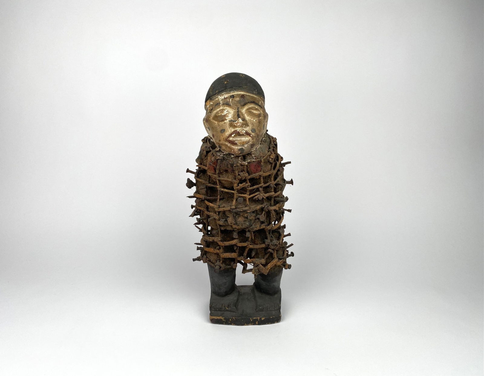 A carved Nkisi Nkondi power figure, representing a human form and traditionally associated with: A carved Nkisi Nkondi power figure, representing a human form and traditionally associated with Central African spiritual and judicial practices. The figure features a painted face and is densely embe