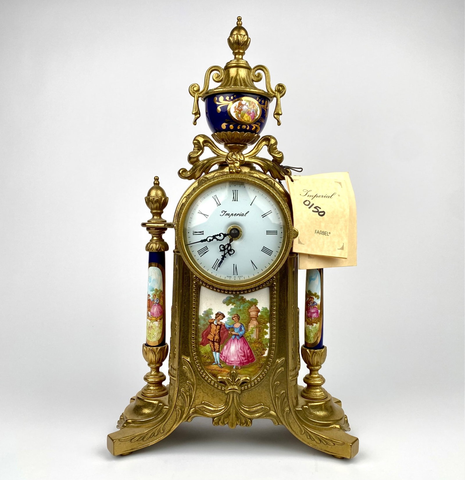 Farbel Imperial gilt metal mantel clock featuring a white enamel dial with Roman numerals and ornate: Farbel Imperial gilt metal mantel clock featuring a white enamel dial with Roman numerals and ornate black hands. Delicately hand-painted porcelain panels and columns depict figures in 18th-century at