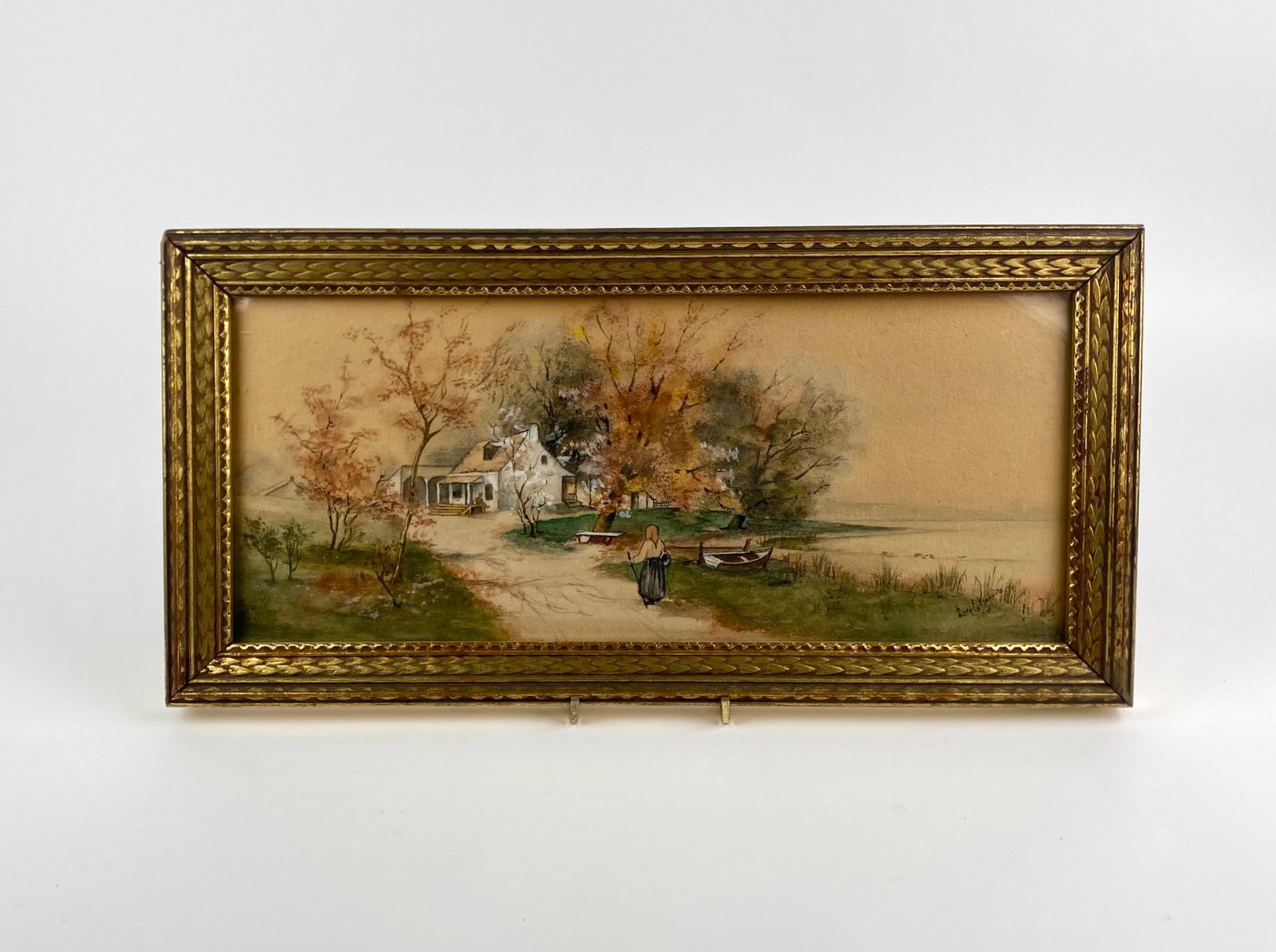 Framed Landscape Watercolor Signed Lury E. Koppitz, Dated 1908: Framed watercolor landscape depicting a rural scene with a cottage set among trees in autumn foliage, a single figure walking along a path, and small boats resting at the water’s edge. The work is