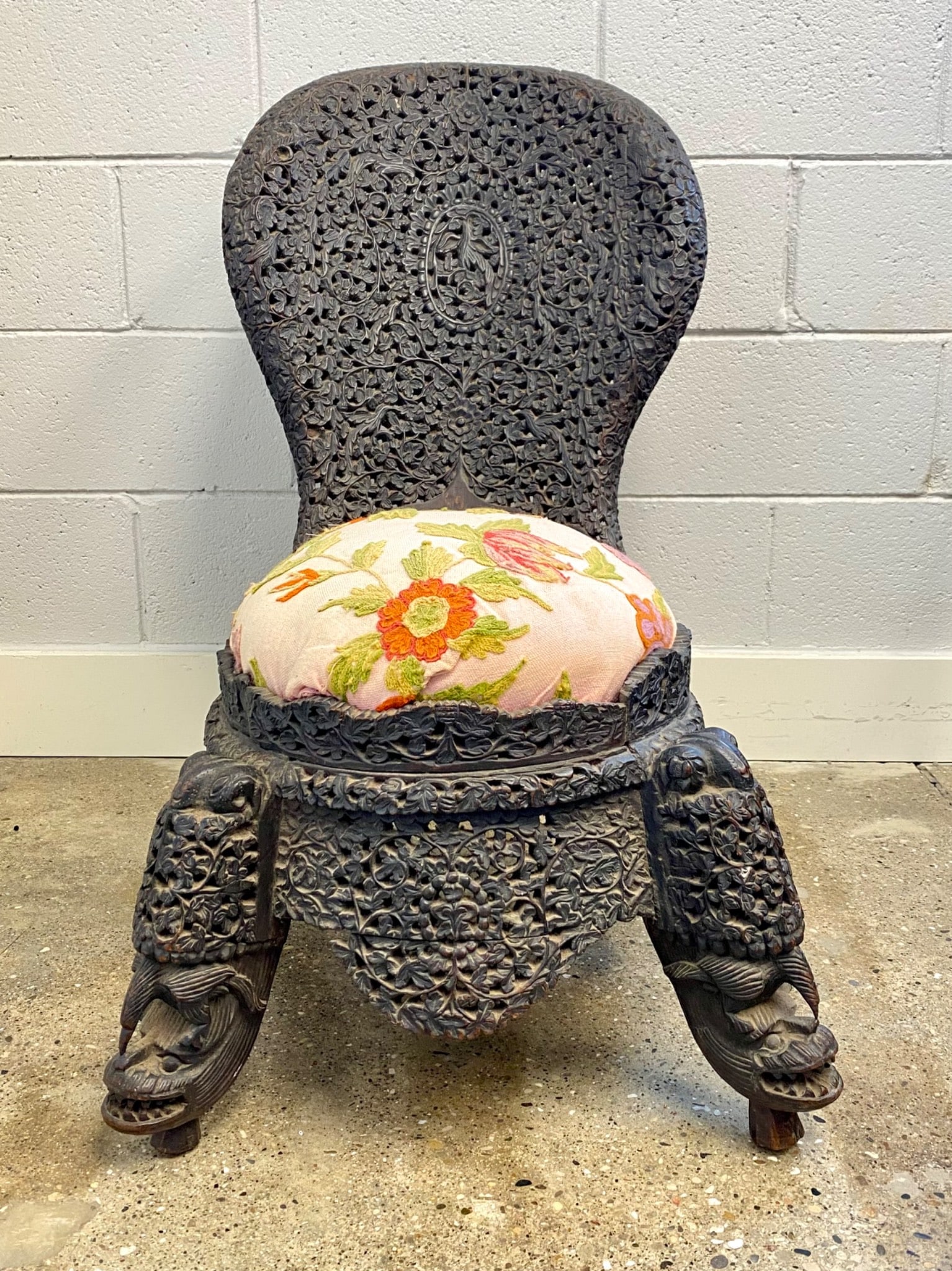 Early 20th century Indian carved wooden chair featuring a high back and detailed floral and vine: Early 20th century Indian carved wooden chair featuring a high back and detailed floral and vine patterns throughout the design. The chair includes a floral embroidered seat cushion in vivid colors