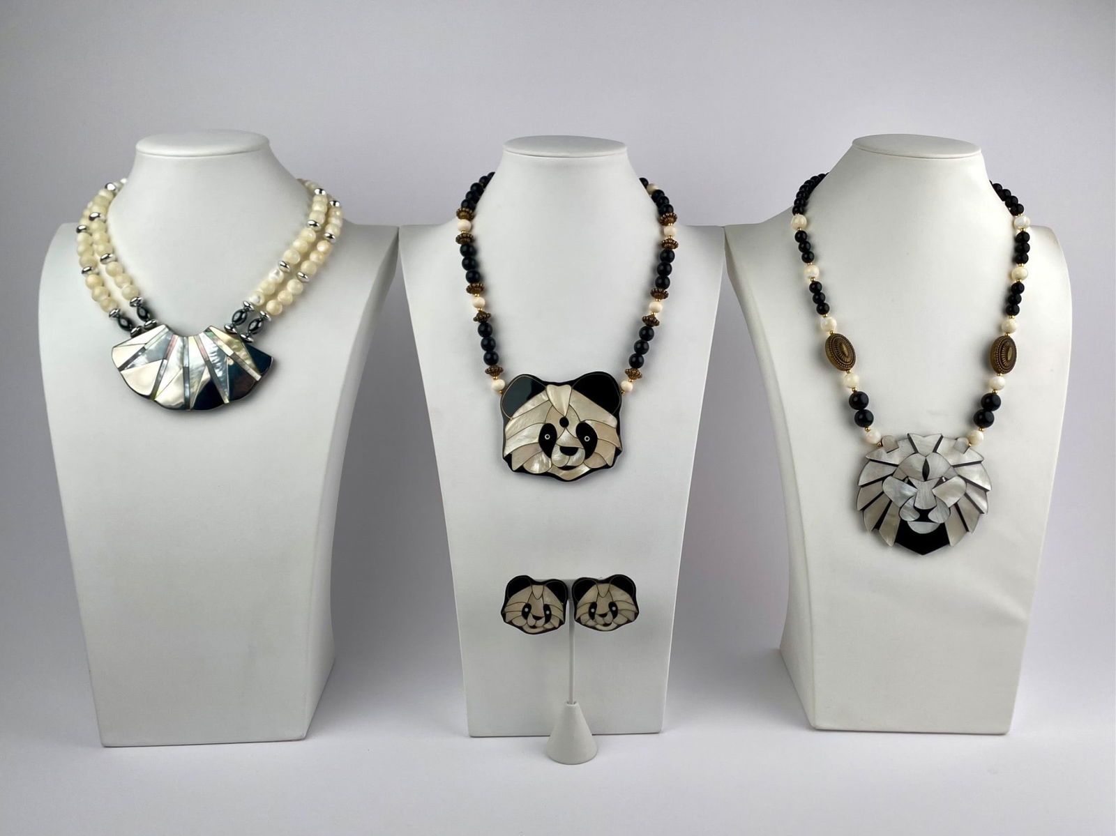 Lot includes four pieces of costume jewelry by Lee Sands. The set features three statement necklaces: Lot includes four pieces of costume jewelry by Lee Sands. The set features three statement necklaces with carved pendants and one matching pair of clip-on earrings. Included are a panda-form pendant