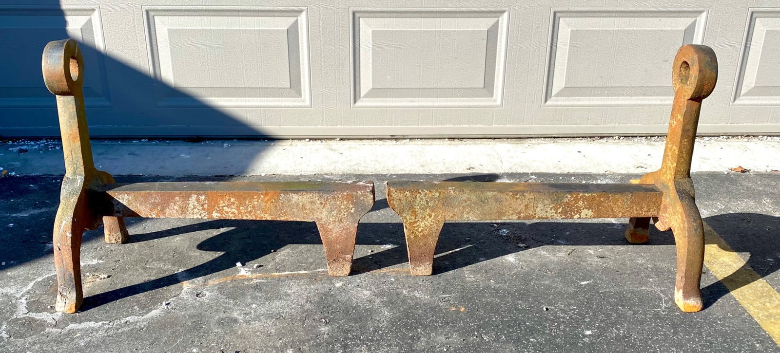 Pair of extra-large cast iron andirons featuring substantial construction and a rustic patina. They: Pair of extra-large cast iron andirons featuring substantial construction and a rustic patina. They include heavy-duty legs and horizontal supports, with an integral circular design at the top of each