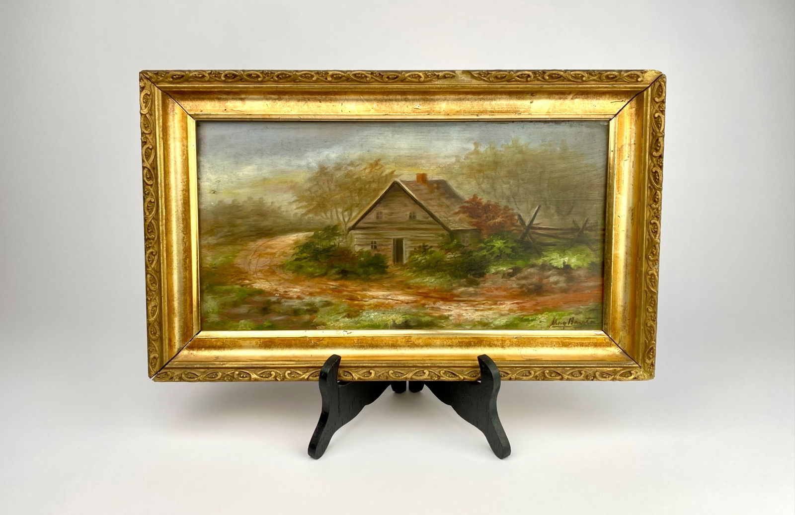 Early 20th Century American Landscape Oil Painting, Signed May Banta: Early 20th century oil painting depicting a rustic house set amidst foliage and a winding path. Signed by artist in the bottom right corner, May Banta. The gilded frame features ornate detailing and