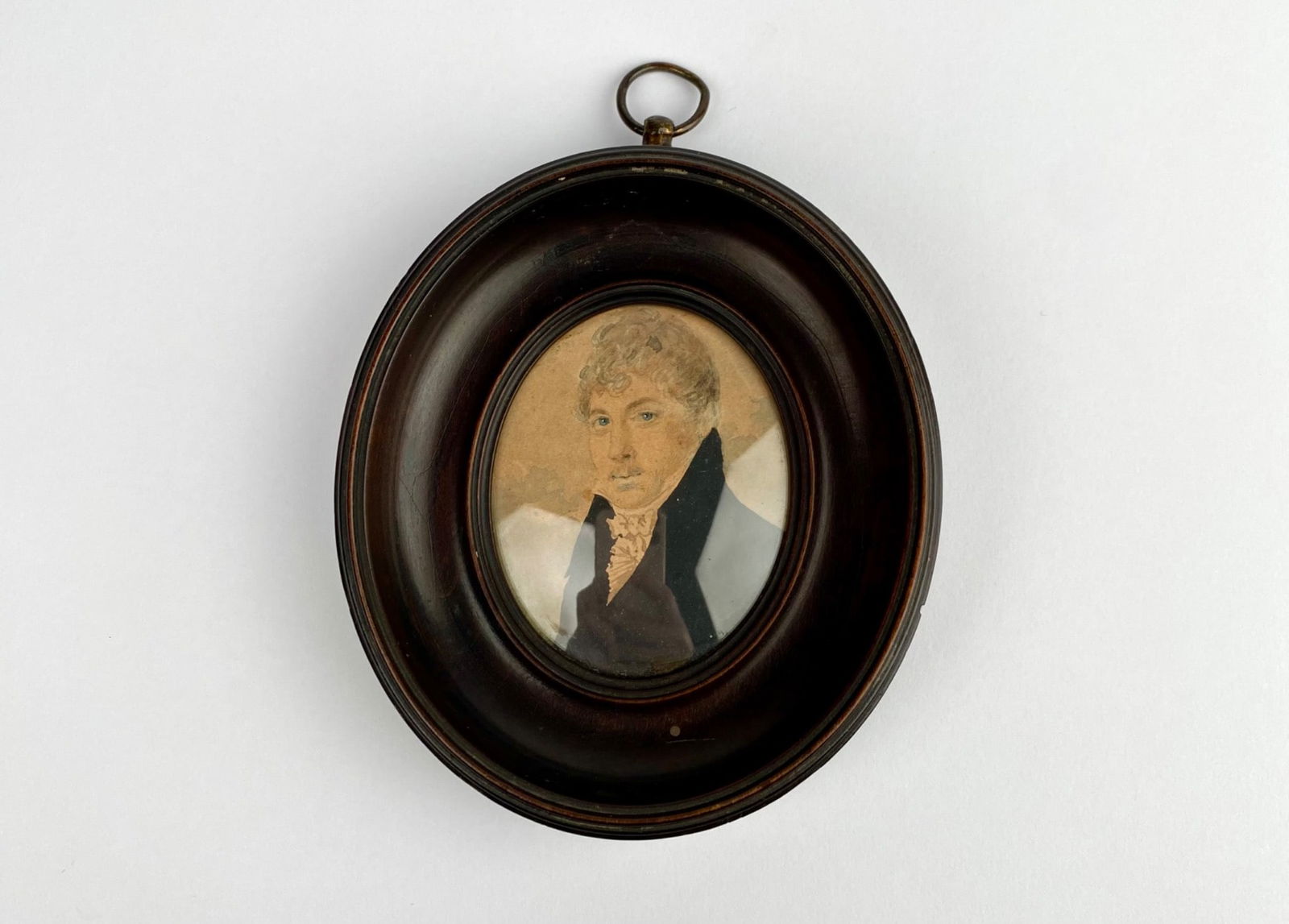 19th-century miniature portrait of a gentleman in an oval wooden frame with glass cover. The: 19th-century miniature portrait of a gentleman in an oval wooden frame with glass cover. The hand-painted image features a man in formal attire. The reverse side bears an aged inscription stating, “