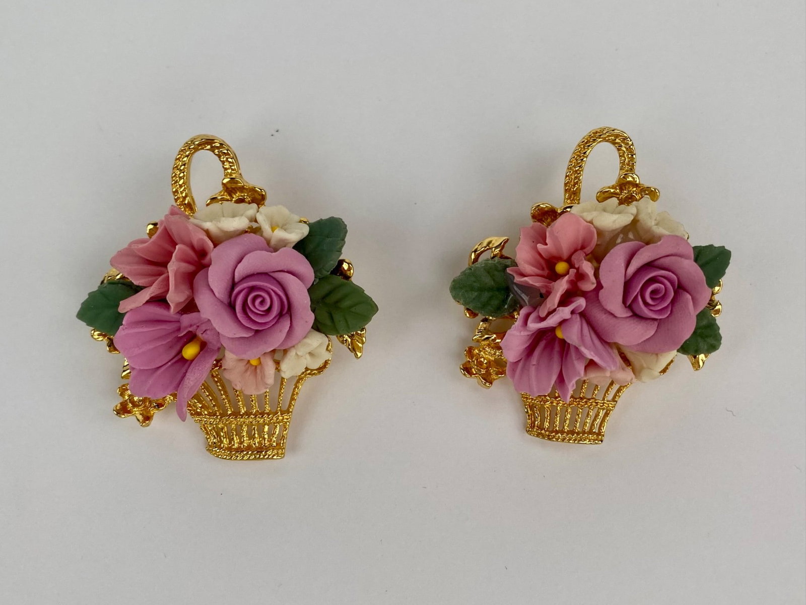 Matching Pair of Vintage Floral Basket Brooches: Matching pair of brooches featuring dimensional floral baskets designs executed in gold tone metal, each adorned with molded pastel flowers and green leaves. Both brooches are fitted with standard pin