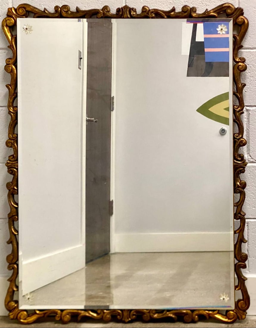 Ornate rectangular wall mirror featuring a gilt wood frame with intricate scrolling details. The: Ornate rectangular wall mirror featuring a gilt wood frame with intricate scrolling details. The mirror includes decorative floral accents at each corner. One floral accent is broken as pictured. Ther