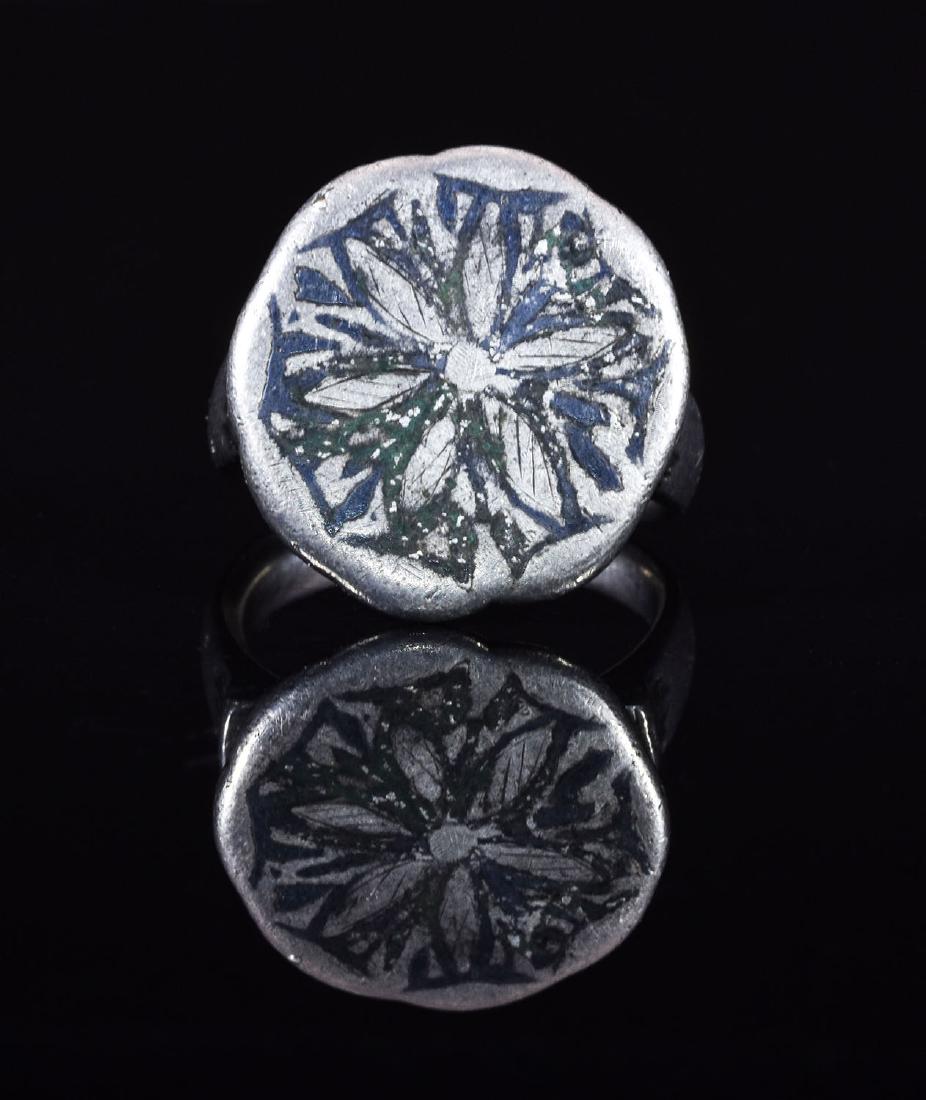 CRUSADERS HOLY LAND SILVER RING WITH NIELLO FLOWER: CA. 1200 AD. Important silver ring from the Holy Lands with oval shaped hoop; applied round bezel ;engraved using a niello ( silver paste technique) with a stylized flower with 6 petals; possibly repr