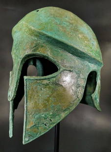 GREEK CORINTHIAN BRONZE HELMET: Ca. 600 Bc. A bronze helmet of the Corinthian type, with curvilinear eye holes that taper to a point, wide nose guard, broad cheek pieces that leave a vertical opening for the mouth, curved projection