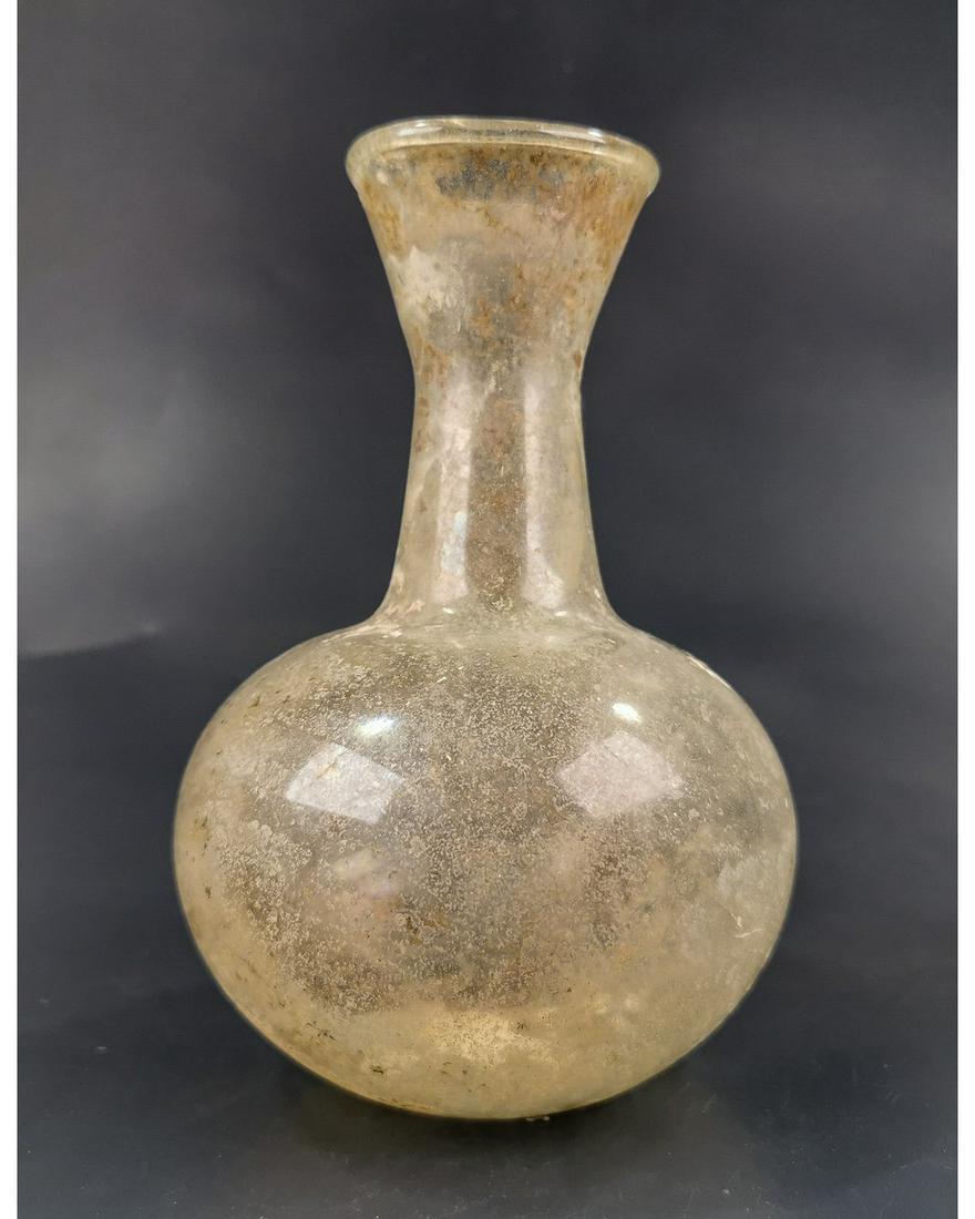ROMAN UNGUENTARIUM GLASS BOTTLE: Ca.100 AD. Ancient Blown Glass bottle with bulbous body, a tall neck and a wide flared spout.Beautiful silver iridescent surface patina.Good Condition; Intact, but with crack.Size: 140x100mm; 5.51x 3.