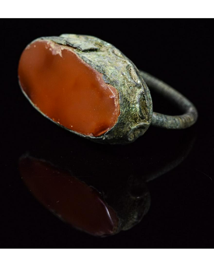 MEDIEVAL BRONZE RING WITH CARNELIAN GEM: Ca.1400 AD. A bronze Tudor Period finger ring with ellipsoid cell to the bezel and inset carnelian cabochon, rope detailing to the rim, flat-section hoop. Good condition; wearable; D:21mm/L:32mm; UK W