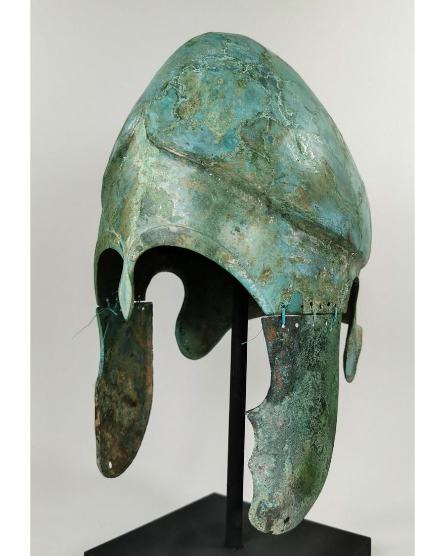 RARE GREEK HOPLITE CHALCIDIAN HELMET: Ca. 400 BC. Attractive Greek Chalcidian Hoplite Helmet with cheek-guards on a custom made stand. The Chalcidian helmet was popular in Greece in the fifth and fourth centuries BC, as well as the southe