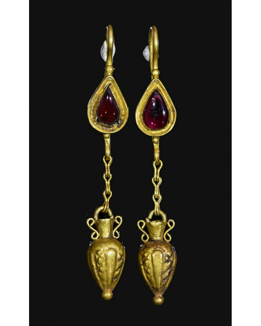 PAIR OF ROMAN GOLD AMPHORA EARRINGS WITH GARNETS: Ca.100 AD. A pair of gold earring with drops in the shape of amphora attached to chains; clasp sets with a garnet cabochons in teardrop shape; Good condition; wearable. 53mm; 2.0882 in; 6.3g; Provenan