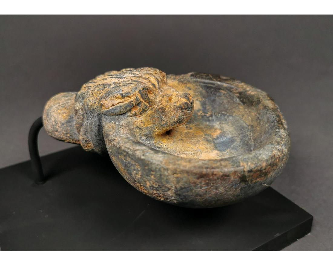 BACTRIAN SCHIST STONE OIL LAMP: Ca.2000 AD. An interesting Bactrian stone leaf-shaped oil lamp with a carved lion head. Good condition, on a custom stand; Size:85mmx120mm;689g Provenance: From an old British collection formed in the