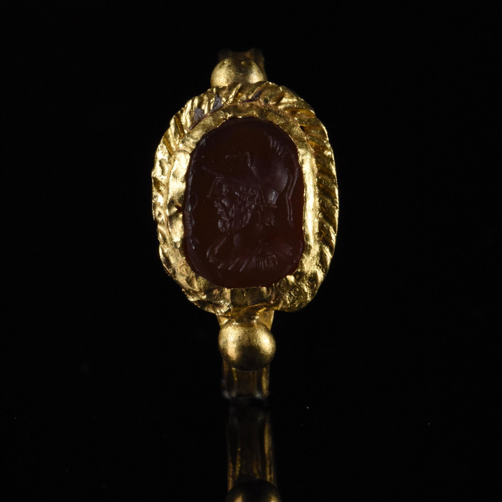 ROMAN GOLD INTAGLIO RING WITH GOD MARS: Ca.100 AD, Roman. Well-preserved gold intaglio ring comprising circular hoop with incised decoration and applied spherical baubles. The raised bezel comprises corded border and a red stone intaglio (p
