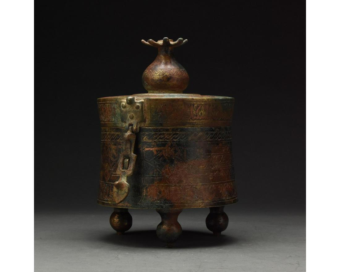MEDIEVAL SELJUK BRONZE LIDDED VESSEL WITH CALIGRAHY: c. 1100 AD. Medieval Seljuk or later. Bronze vessel comprising three elegant feet which support a cylindrical drum with a hinged lid. The lid supports a stylised tower or tree motif. The exterior of t