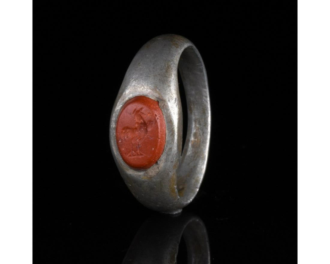 ROMAN SILVER INTAGLIO RING WITH ROOSTER: 1-300 AD, Roman. Silver ring with a D-shaped hoop formed from a thick, flat-sectioned, flaring band bearing a red gem intaglio with an incised rooster. This item probably served as a signet ring used 
