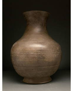 CHINA, HAN DYNASTY LARGE POTTERY VESSEL WITH TAOTIE: Ca. 206 BC - 220 AD. Han Dynasty. Beautiful ceramic vase with a beige fabric and glossy dark brownish-grey slip. The vase comprises a flaring rim, elongated neck and a round globular body supported