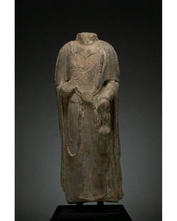 CHINA, NORTHERN QI DYNASTY STONE TORSO OF BUDDHA: 549 - 577 AD. Northern Qi Dynasty. Grey stone torso of a standing Buddha, without a head which would probably have originally been in precious metal. The torso stands upright, wears a light,