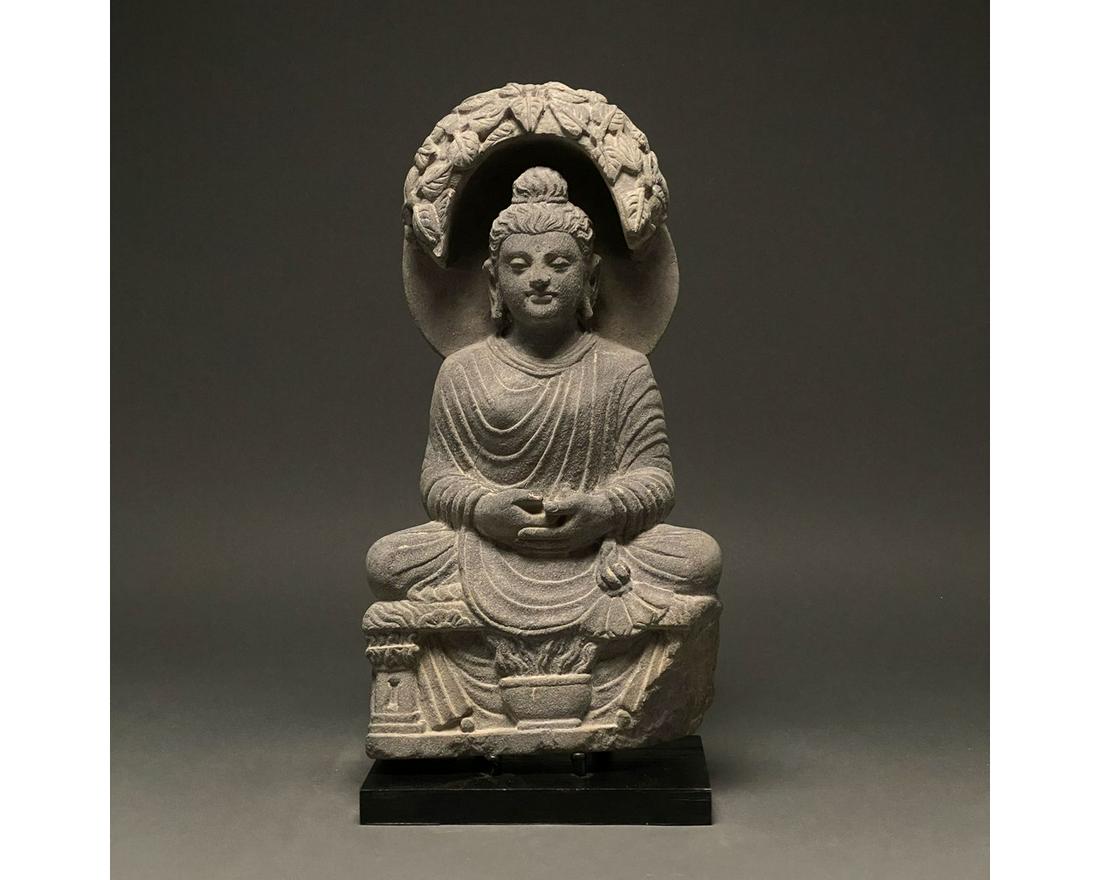 GANDHARA SCHIST STONE FIGURE OF SEATED BUDDHA: 100-300 AD. Gandharan. A grey schist figure of a seated Buddha. He is depicted wearing a flowing robe and a topknot (ushnisha). There is an urna on his forehead, and he is characterised by his arched 