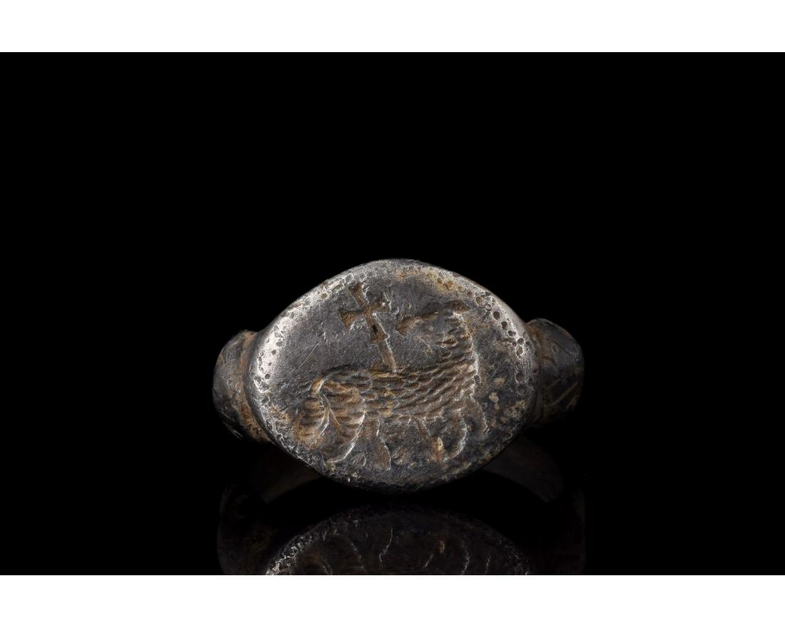 RARE MEDIEVAL SILVER RING WITH AGNUS DEI: 1100-1300 AD. Medieval. A rare silver ring with a circular hoop, scalloped shoulders and elliptical plate bezel bearing an engraved lamp with a cross, which represents the Agnus Dei (Lamb of God). The