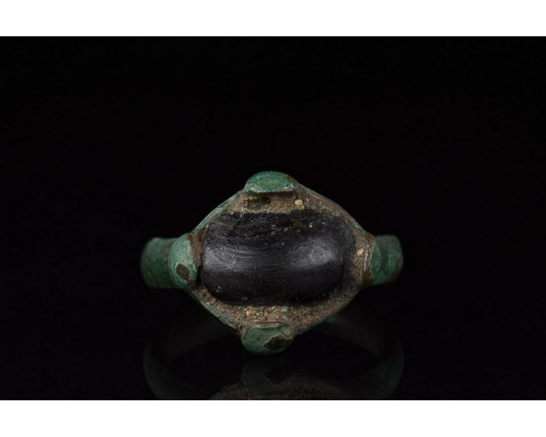 VIKING ERA BRONZE RING WITH LARGE DARK GEM: 700-1100 AD, Viking Age. Bronze ring with a circular hoop, and a lozenge shaped bezel onto which is mounted a large, oval dark coloured gem. This simple yet elegant ornament may have belonged to a Vik