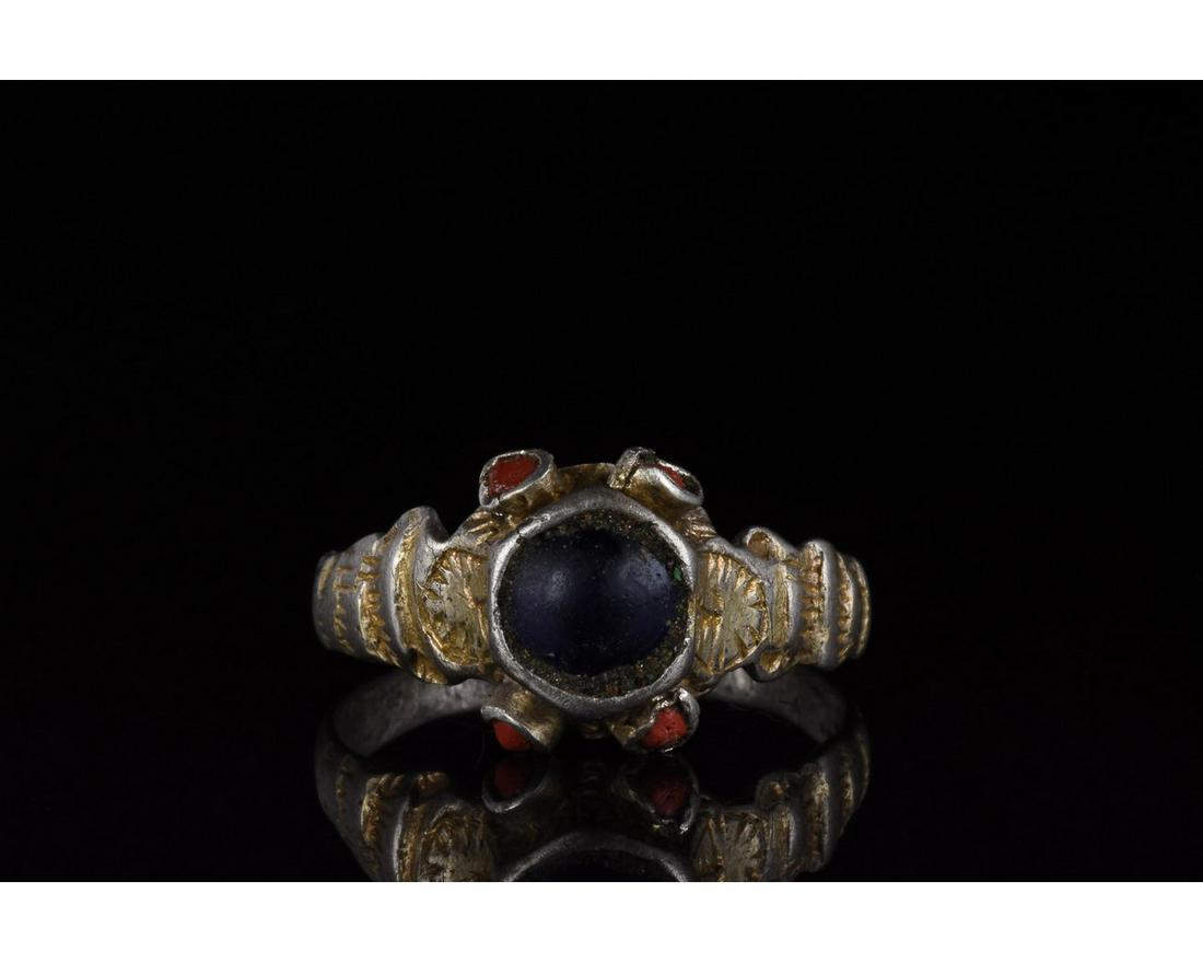 MEDIEVAL SILVER GILT RING WITH STONES: 1100-1300 AD. Medieval. A silver gilt ring with a circular hoop scalloped shoulders and trumpet bezel comprising a large black cabochon gemstone framed by four smaller red cabochon stones. Excellent c