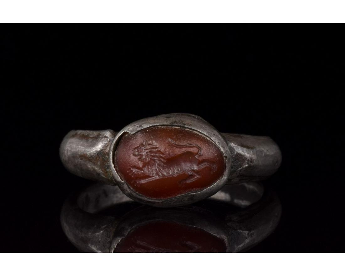 ROMAN SILVER INTAGLIO RING WITH LION: C. 100-300 AD. Roman. Silver ring comprising circular hoop a raised elliptical bezel with a red gem setting. The setting bears an engraving depiction of a running lion. This item probably belonged to 