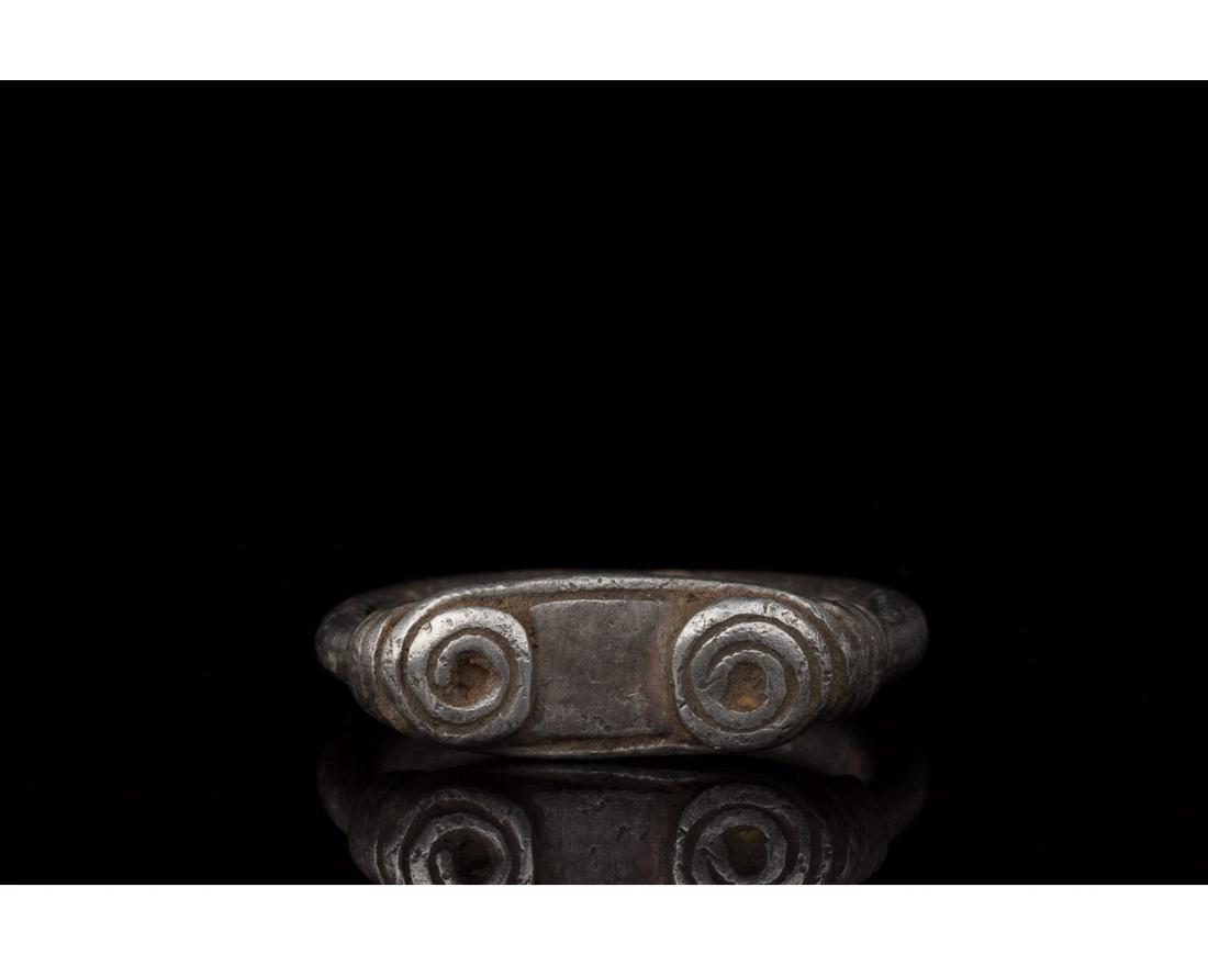 VIKING SILVER COILED RING: 700-1100 AD, Viking Age. A silver with a D-shaped hoop, and elliptical bezel affixed to the hoop by applied coils of silver with trailing ends which wind down the shoulders and are intended to evoke t