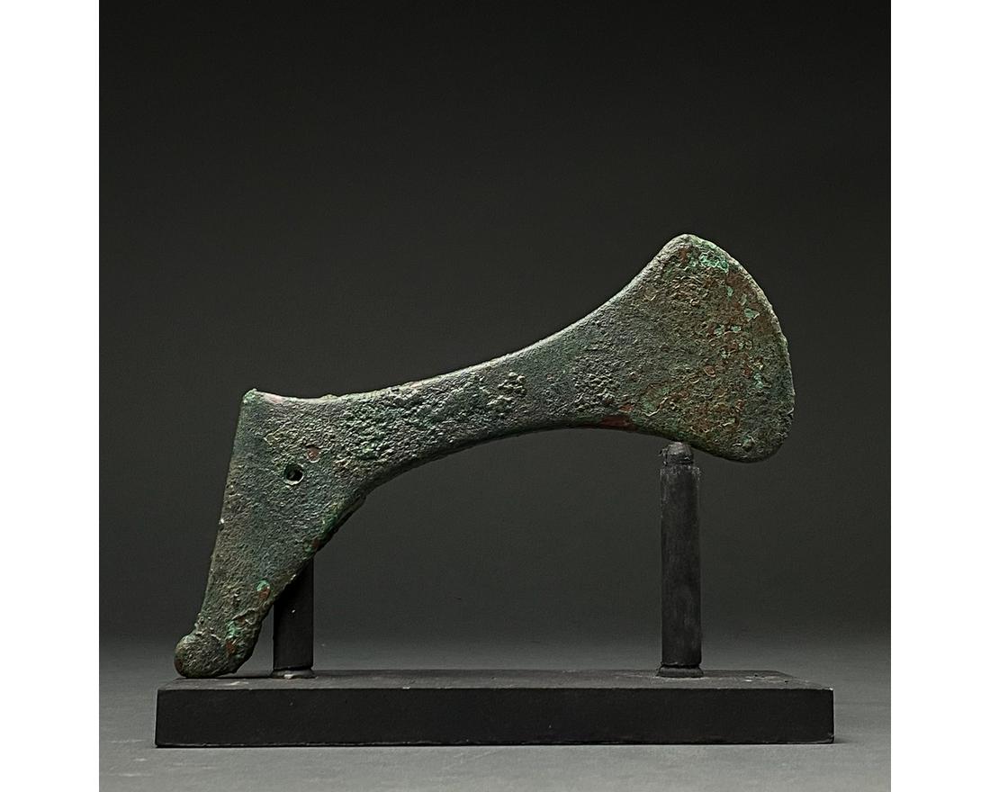 BRONZE AGE BATTLE AXE ON STAND: C. 2000-700 BC. Bronze Age. A bronze battle axe with a short, curved blade, tapering cheek and wedge-shaped butt. Bronze weaponry production flourished from the 2nd millennium BC to about 700 BC when 