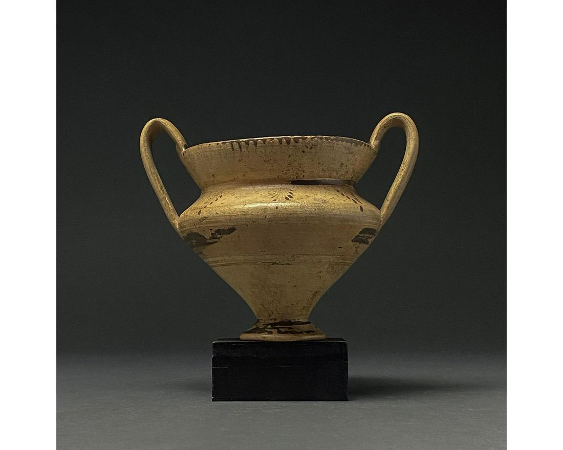 GREEK DAUNIAN TERRACOTTA VESSEL WITH HANDLES: 600-200 BC. Apulia. A Daunian terracotta cup with a flaring rim, carinated body, ring foot, and two high, ear-shaped handles. Several bands of brown painted decoration are visible on the body and neck