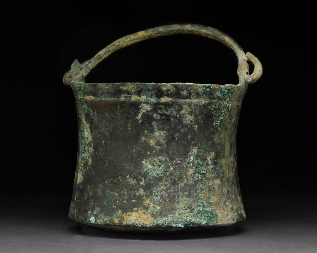 ROMAN BRONZE SITULA: Ca. 100 AD. Roman. A bronze situla with gently curved concave sides, two riveted attachment plates with a loop at the rim to take the slender parabolic handle which is threaded through them and twiste
