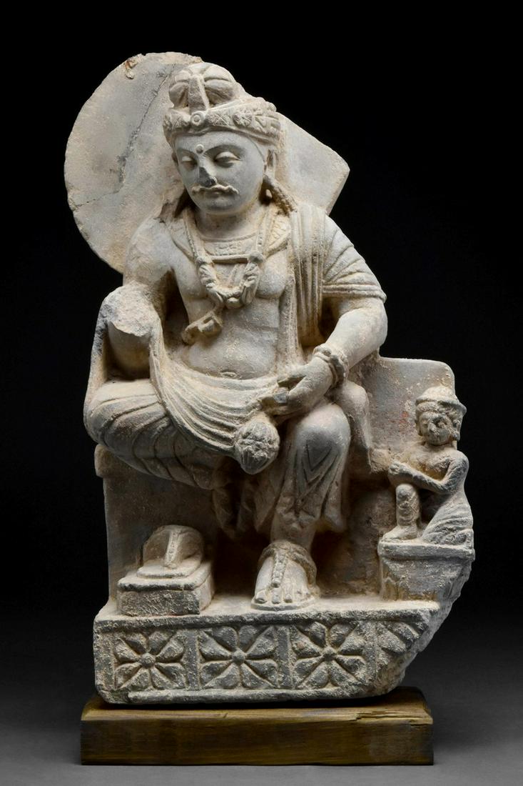 GANDHARAN RELIEF OF BODHISATTVA SHAKYAMUNI: Ca. 200-300 AD Seated with his left knee bent on a plinth with lotus flowers, shadowed by a wide nimbus affirming his divinity, the heavy robe wraps around his athletic physique with dramatic folds re