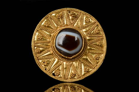 HELLENISTIC GOLD BROOCH WITH AGATE EYE: Ca. 300-100 BCHellenistic PeriodA finely rendered Greek Hellenistic gold disc-shaped brooch/pendant, hammered from thin gold, with an agate eye to the centre, along the brooch thirteen pyramid shaped