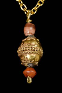 EASTERN GREEK GOLD PENDANT: Ca. 400-300 BCA gold pendant in the form of a globe with centre panel band of decoration, inbetween two carnelian beads. The pendant attached with a gold later necklace.Size: L:29.3mm / W:9.8mm;