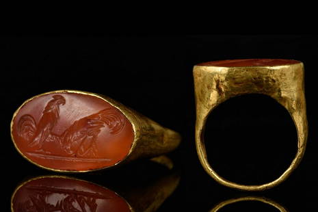 ROMAN CARNELIAN INTAGLIO WITH FIGHTING COCKERELS: Ca. 100-200 ADA substantial gold ring with hollow hoop widening to the shoulder; oval bezel carnelian intaglio engraved with two fighting cockerels.For similar see:Chadour, A.B. Rings. The Alice and