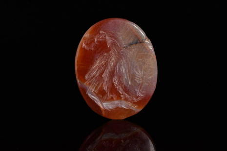 ROMAN CARNELIAN INTAGLIO OF AN EAGLE: Ca. 200 ADAn oval shaped intaglio with an eagle. The bird of prey is positioned above a circular altar, holding a laurel wreath in its beak, and a palm branch with the legs. The animal is facing