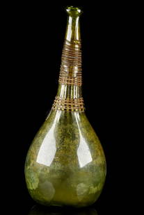 SAFAVID GLASS SADDLE BOTTLE / VASE WITH RIBBED NECK: Persia, Ca. 17th century AD An impressive greenish glass bottle featuring a round body sitting upon a concave base, with a sloped shoulder that gently tapers to a long tubular neck finished with a fla