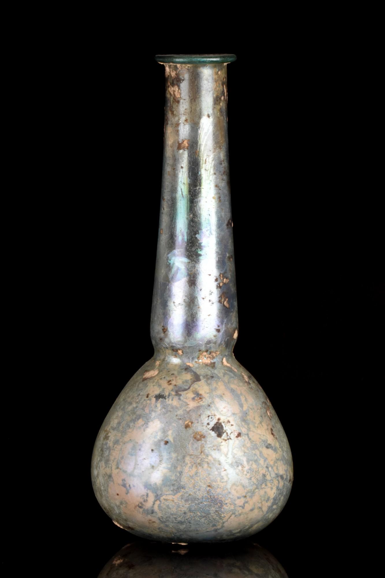 ROMAN GLASS UNGUENTARIUM: Roman Empire, Ca. 1-300 AD An elegant glass unguentarium featuring a piriform lower body leading to a long, narrow neck with a round folded rim. This beautiful glass vessel features some iridescence t