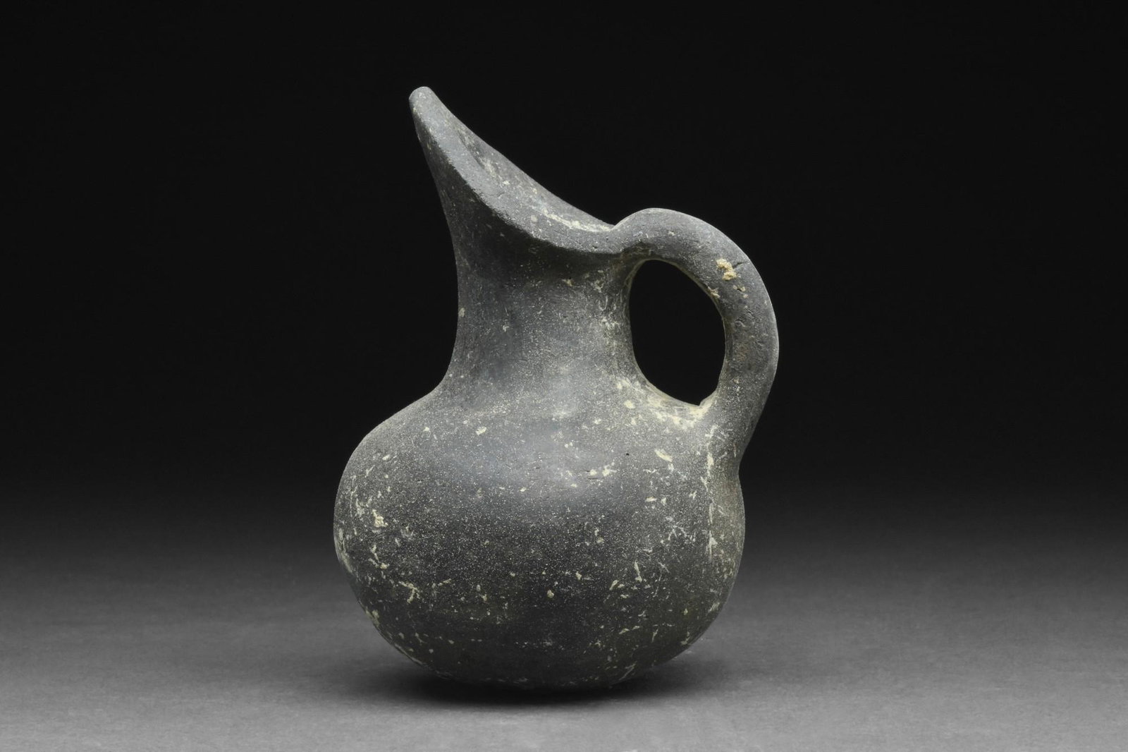 ANATOLIAN YORTAN POTTERY JUG: Ca. 2700-2400 BC.A wheel-thrown blackware jug with a spherical-shaped lower body, sloped shoulder, long, wide-beaked spout, and a curved, strap handle. For a similar example, see The Metropolitan Muse