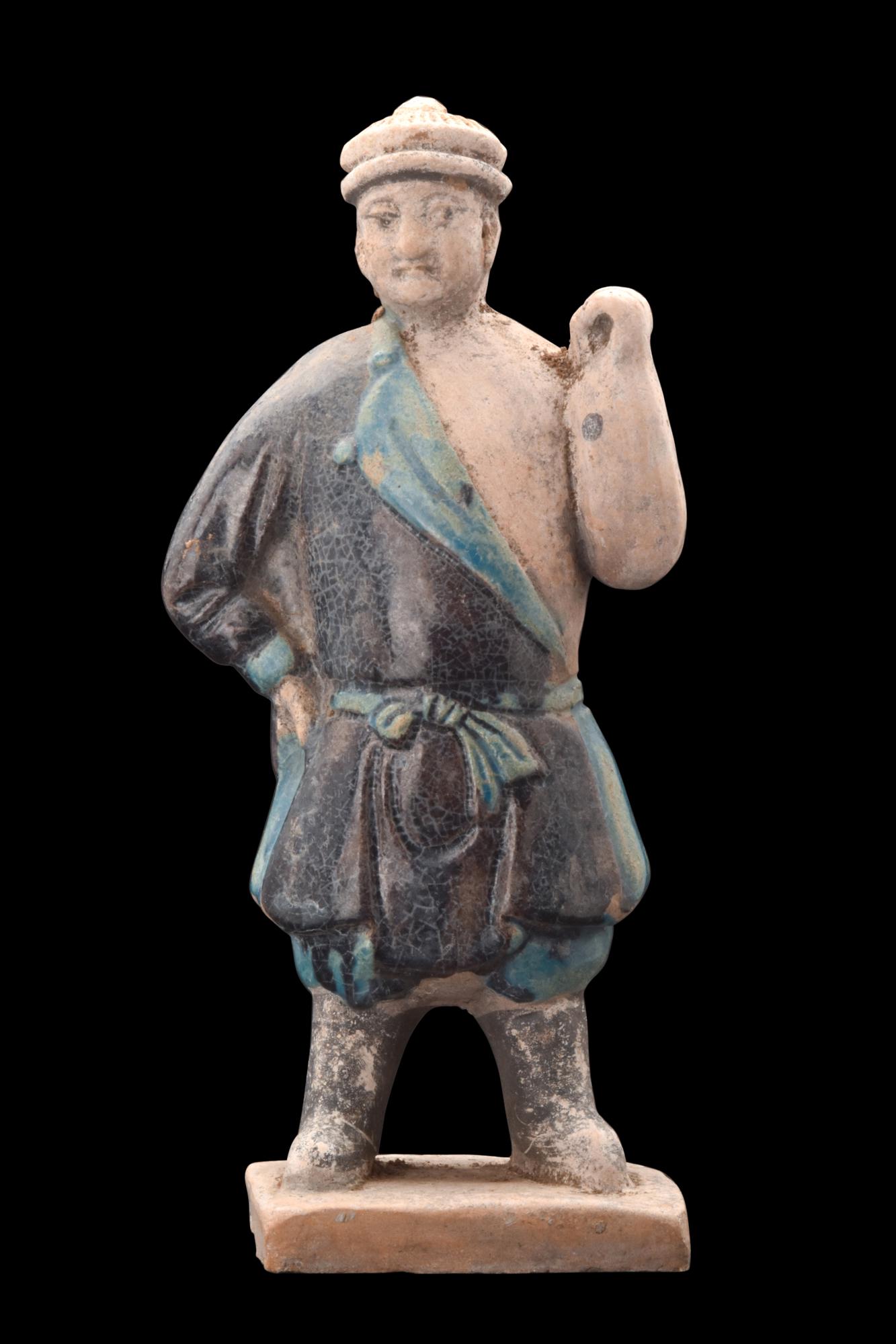 CHINESE MING DYNASTY GLAZED TERRACOTTA SEDAN CHAIR CARRIER: Ca. 1368-1644 AD or later . A glazed-terracotta figurine depicting a sedan chair carrier in an upright position, standing atop an integral, small base. The gentleman is dressed in a carefully glazed r