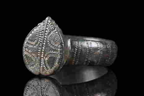 BYZANTINE BRONZE RING WITH SHIELD-SHAPED BEZEL: Ca. 500-600 AD. A bronze ring with a circular hoop, flat on the inside, and slightly rounded on the outside with a raised circular boss at the rear and a lovely decoration composed of several, vertica