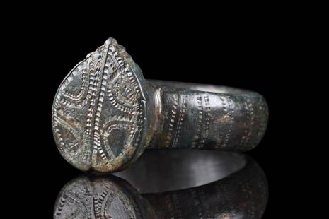 BYZANTINE BRONZE RING WITH SHIELD-SHAPED BEZEL: Ca. 500-600 AD. A bronze ring with a circular hoop, flat on the inside, and slightly rounded on the outside with a raised circular boss at the rear and a lovely decoration composed of several, vertica