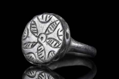 BYZANTINE BRONZE RING WITH FLORAL PATTERN: Ca. 500-600 AD. A beautiful bronze ring with a smooth, circular band supporting a large bezel decorated with a five-petaled floral design. Further incised decoration runs around the perimeter of the b