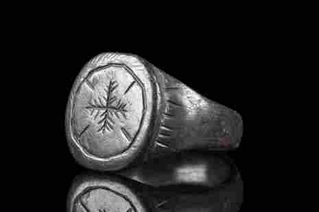 BYZANTINE BRONZE RING WITH CROSS: Ca. 500-600 AD. A bronze finger ring composed of a plain, circular band, that gradually expands to form a circular bezel. The shoulders are decorated with radiating lines and a bezel bears a depiction