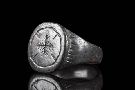 BYZANTINE BRONZE RING WITH CROSS: Ca. 500-600 AD. A bronze finger ring composed of a plain, circular band, that gradually expands to form a circular bezel. The shoulders are decorated with radiating lines and a bezel bears a depiction