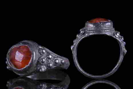 BYZANTINE SILVER RING WITH RED STONE: Ca. 600-800 AD. A silver finger ring of a round, slightly carinated hoop with the shoulders gently flaring outward towards the bezel. Embellishing the shoulders are triangular plaques, which are furth