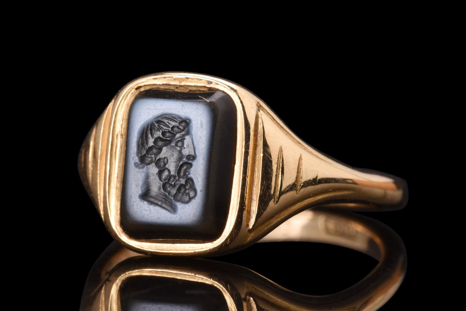 NEOCLASSICAL GOLD RING WITH ZEUS NICOLLO INTAGLIO: Ca. 1800 AD. A gold ring of a thin hoop gradually expanding to form a bezel, which is set with a rectangular-shaped nicollo intaglio, carefully engraved with a right-facing portrait of Zeus. The intag